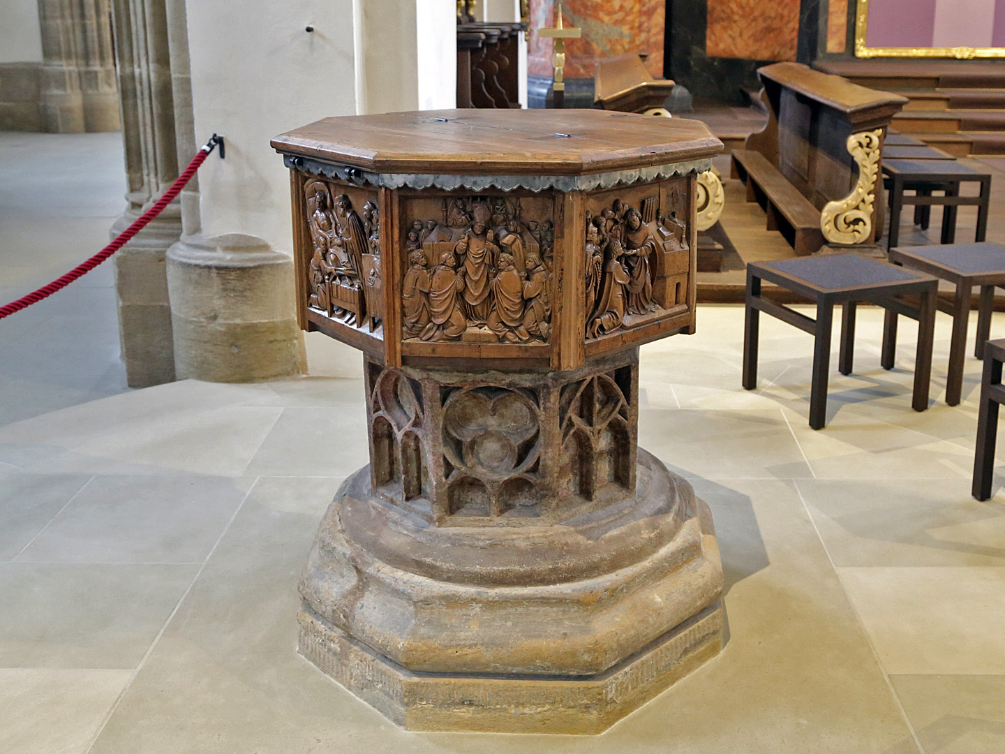 Die Holzverkleidung des Taufsteins zeigt künstlerisch u. a. die Sakramente der katholischen Kirche.